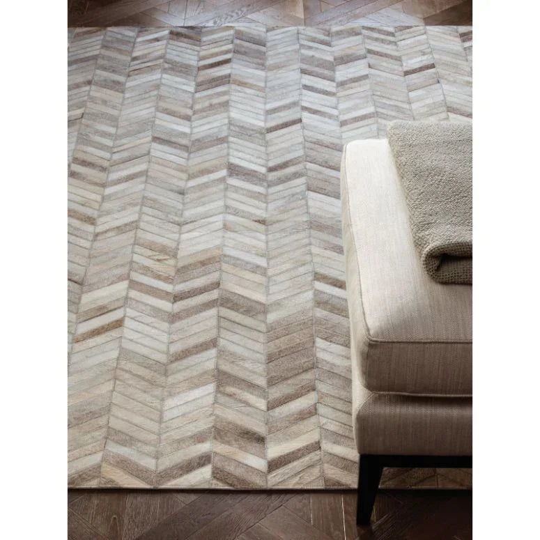 Chevron pattern area rug in neutral tones beside a beige ottoman on wood flooring