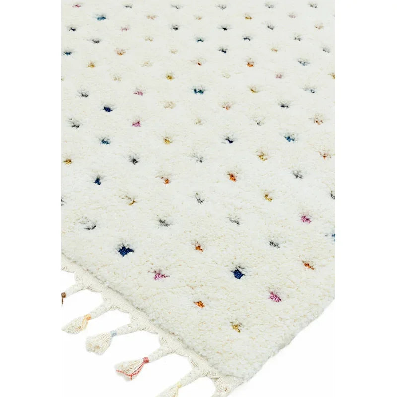 Cream wool rug with multicoloured dot pattern and tasseled edge, close up view