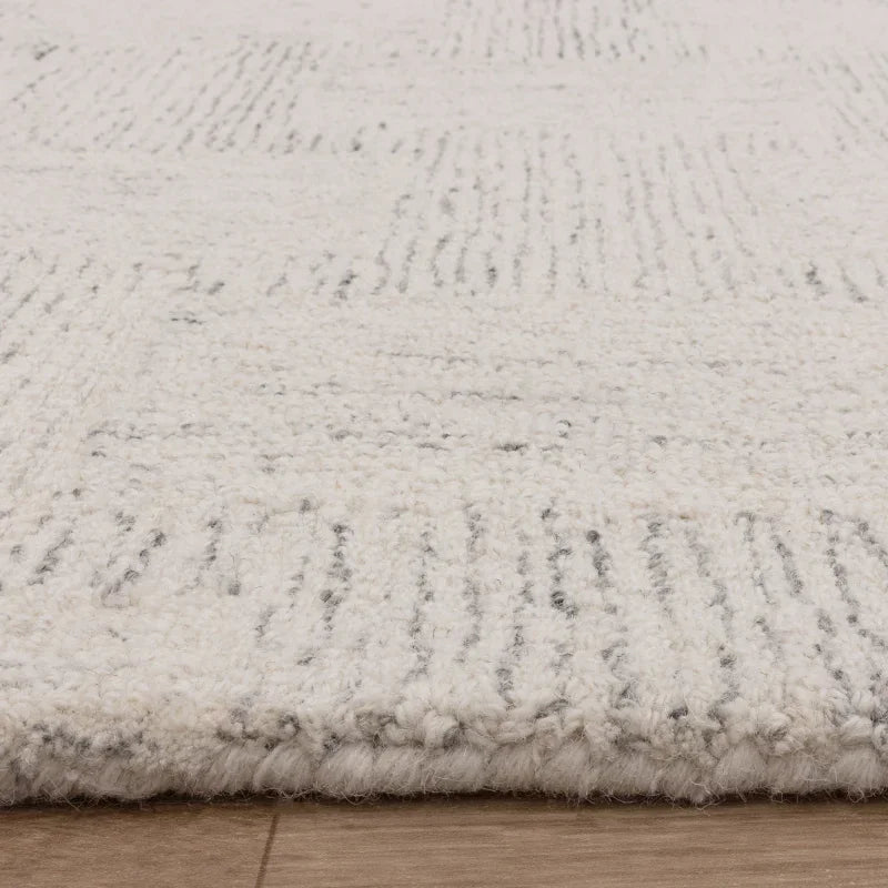 Cream wool rug with subtle geometric pattern on wooden floor, close-up corner view