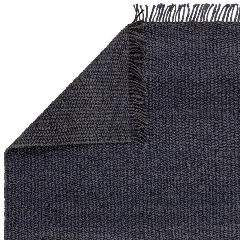 Charcoal woven rug with fringed edge and texture detail shown at corner