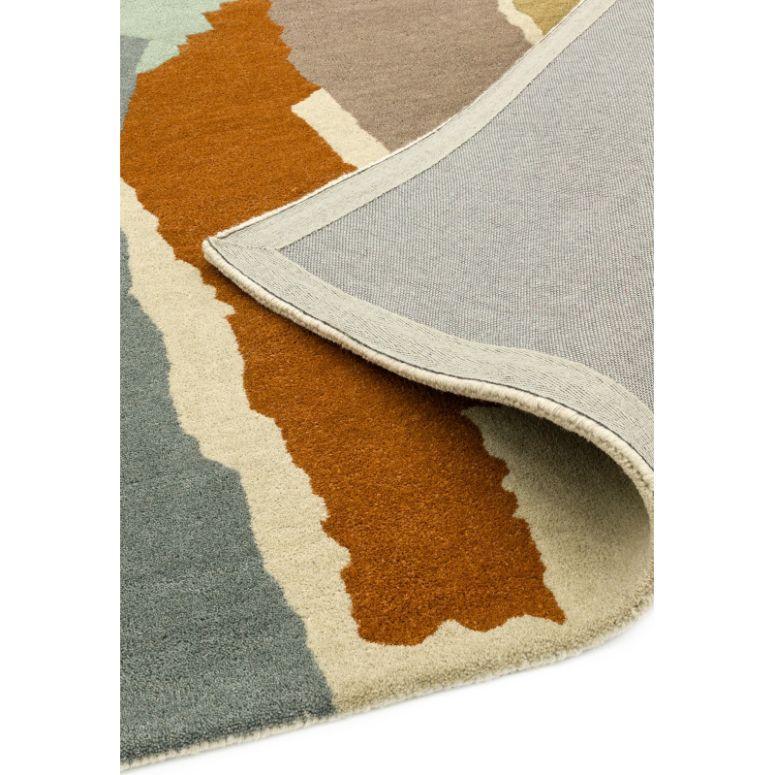 Modern abstract area rug with rust, cream and grey patterns, corner flipped to show backing