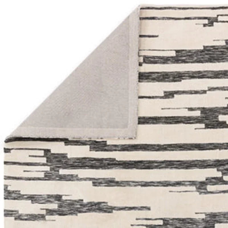Modern area rug with black linear pattern on cream background, corner folded to show backing