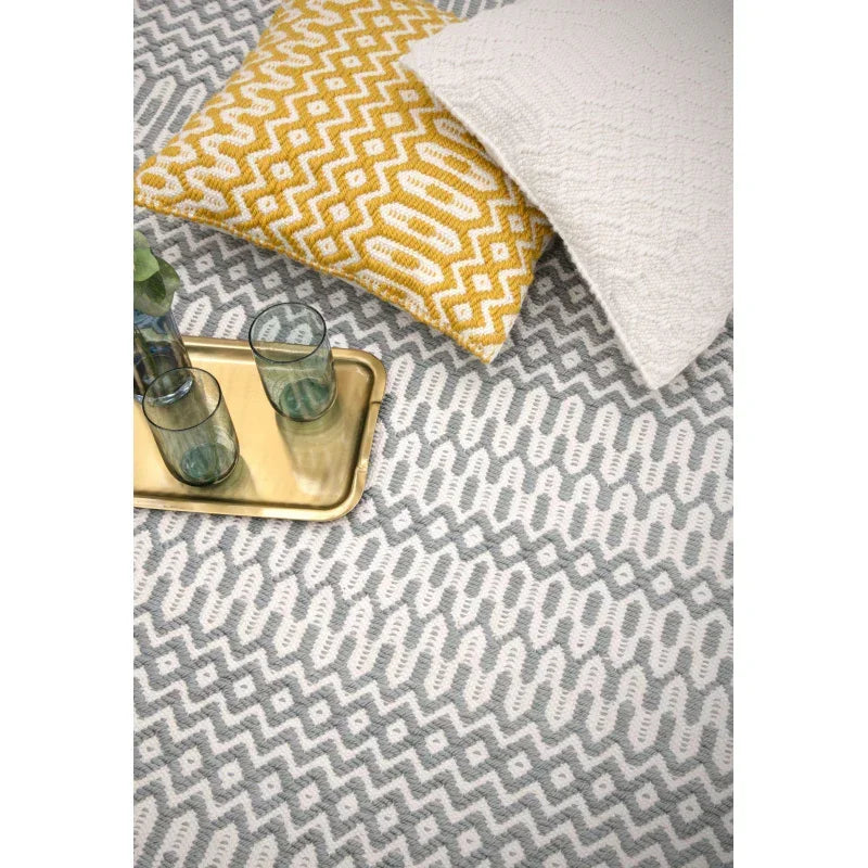 Grey and white patterned area rug with yellow geometric cushion and gold tray with glasses