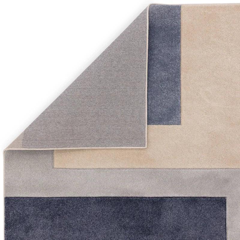 Geometric wool rug in beige, grey, and navy with folded corner showing backing
