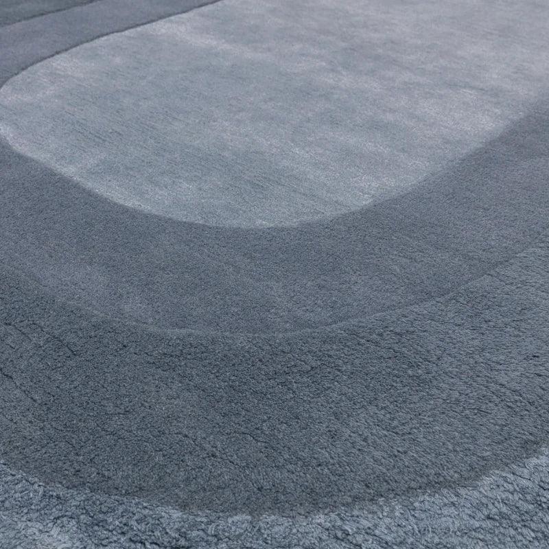 Grey area rug with textured abstract pattern and curved design, close-up angle