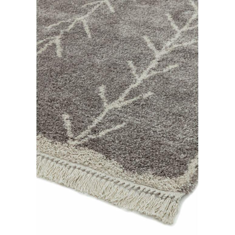 Grey area rug with cream branch pattern and fringed edge corner closeup