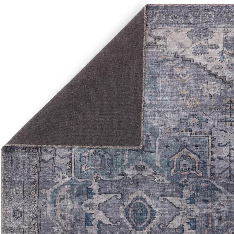 Blue and grey area rug with intricate pattern, corner flipped to show backing