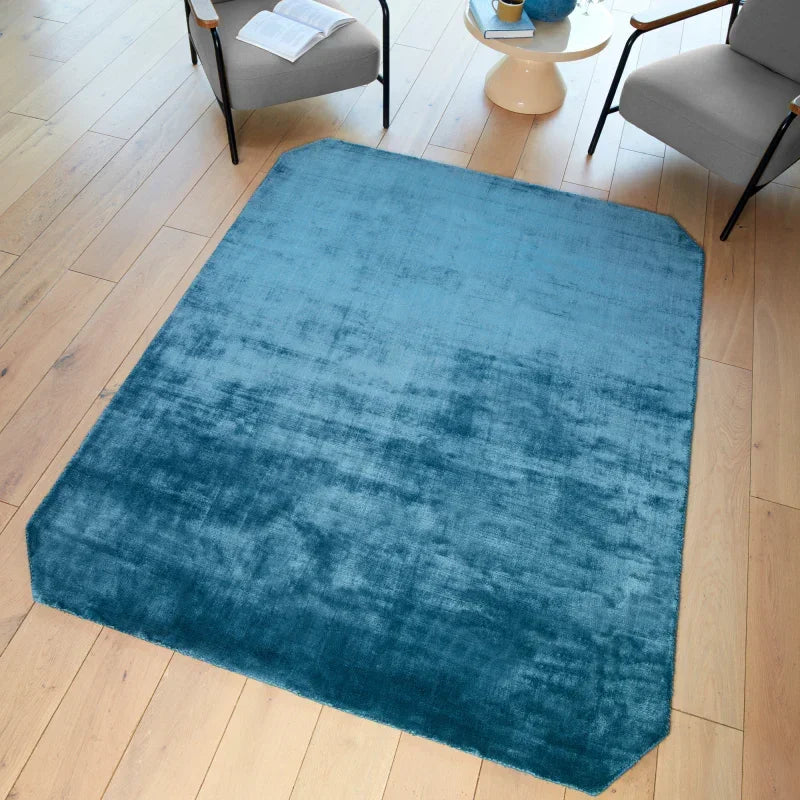 Blue area rug with velvet texture on light wood floor between two modern armchairs