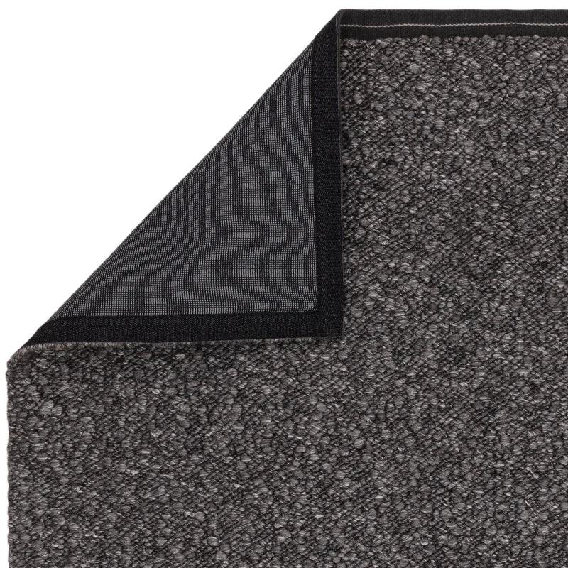 Dark grey textured rug with woven surface, corner flipped to show non-slip backing