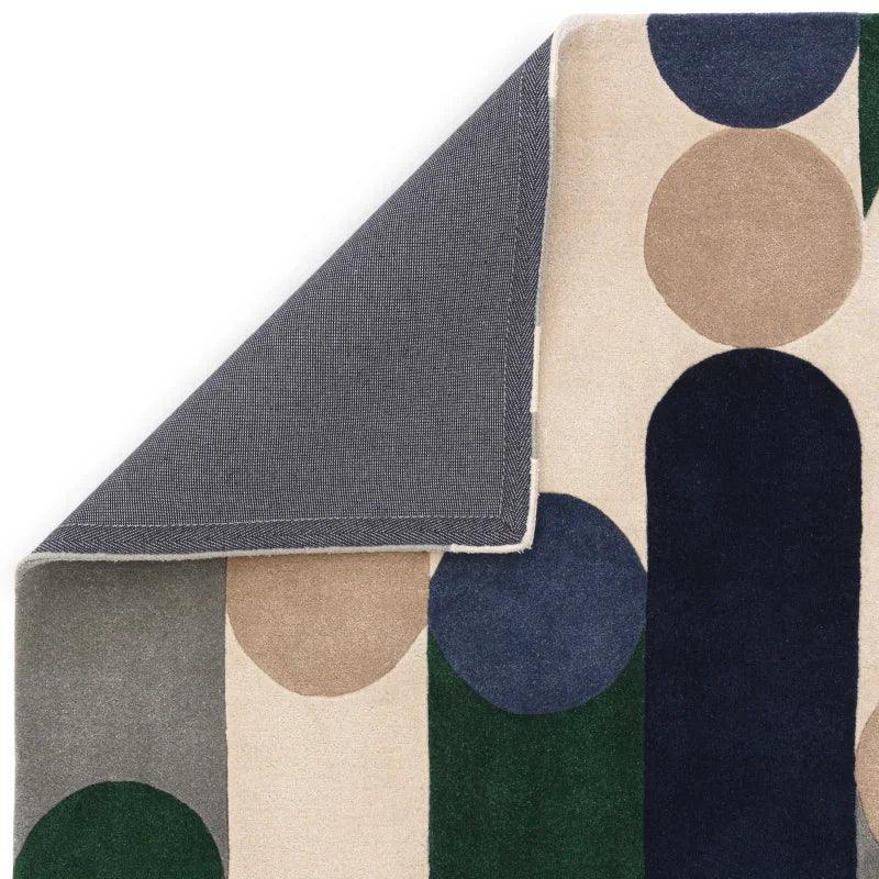 Geometric patterned rug with beige, navy, green, and grey shapes, corner folded over