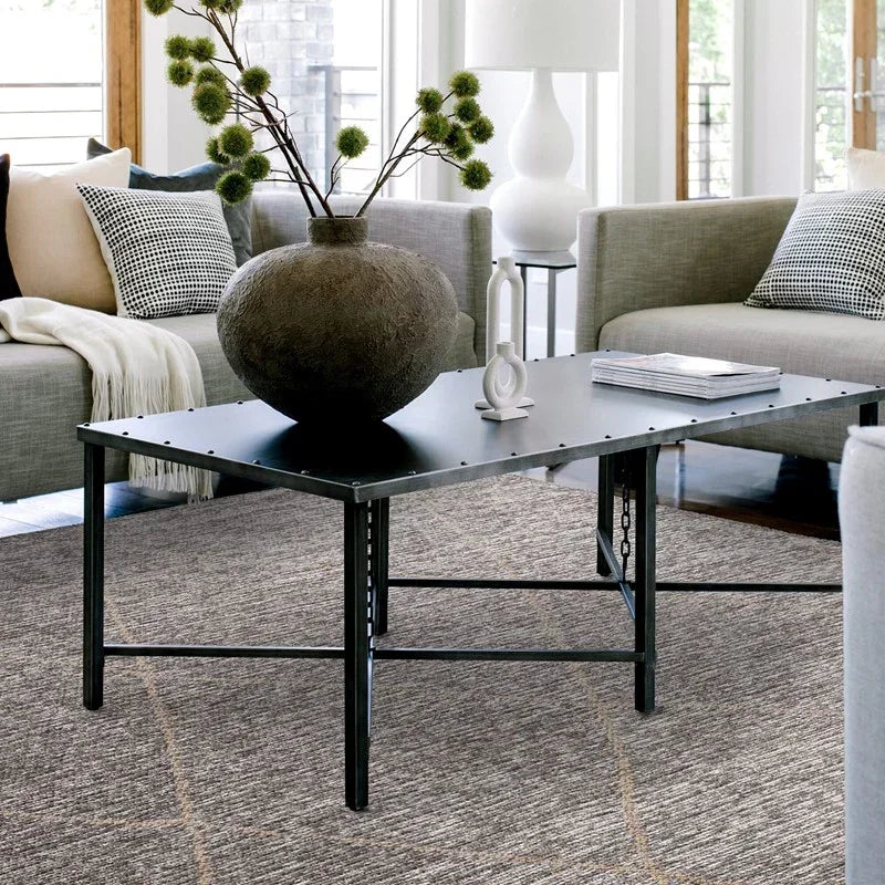Black metal coffee table with decorative vase and books in modern living room with grey sofas
