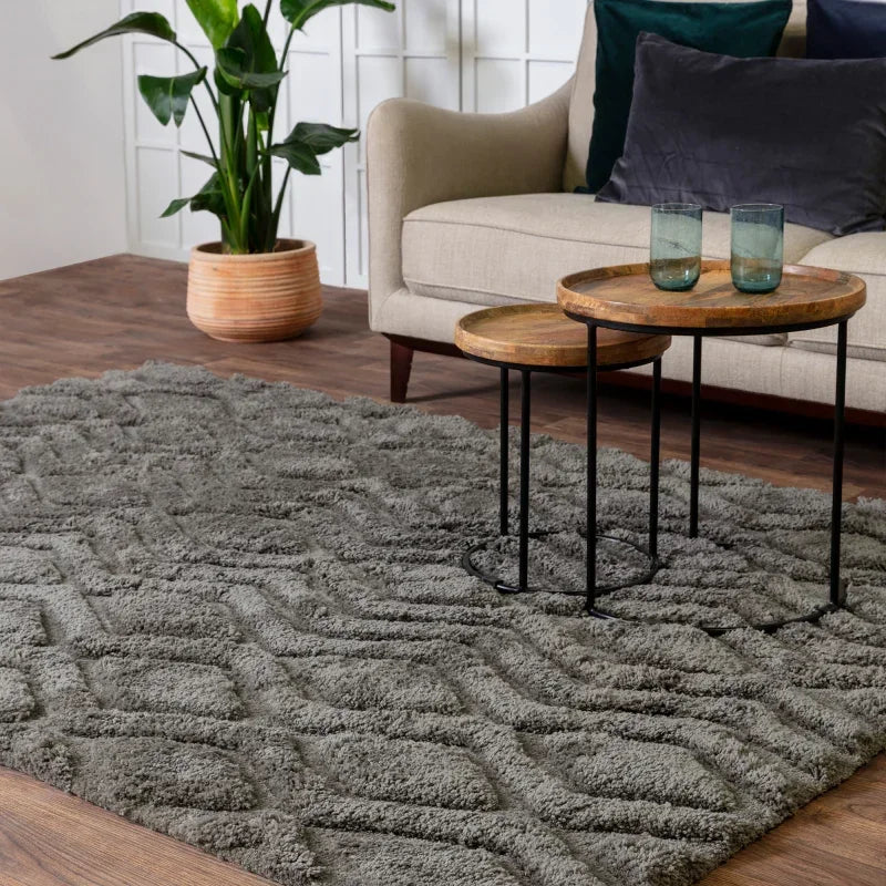 Grey textured rug on wooden floor with nest of tables, beige sofa and green plant