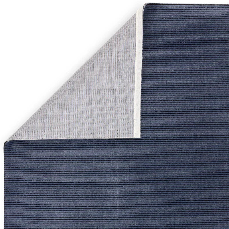 Navy blue textured area rug with corner flipped to show grey non-slip backing