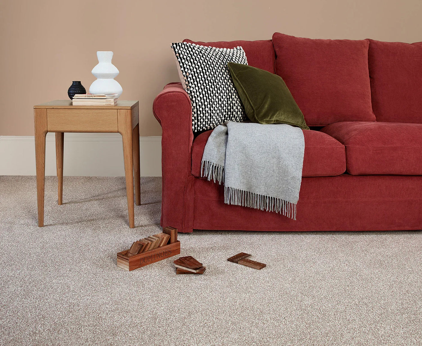 Red fabric sofa with grey throw and patterned cushions on beige carpeted floor