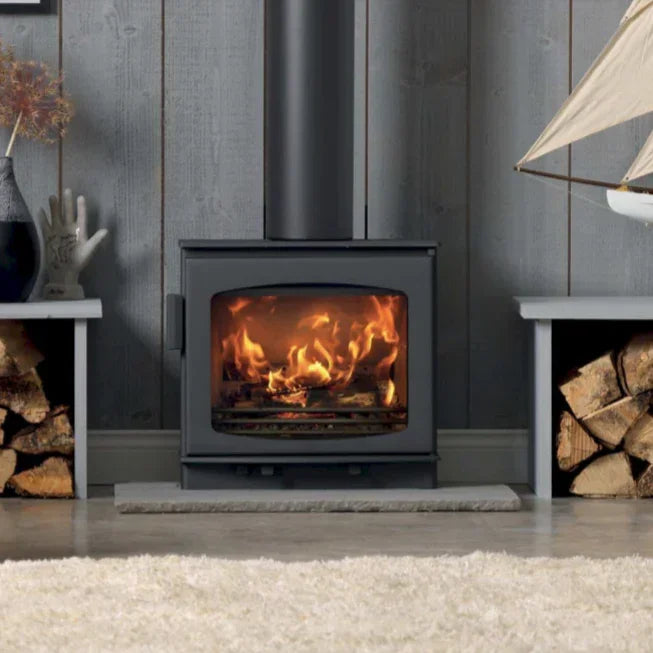Modern wood burning stove with fire, log storage, and grey panelled wall background