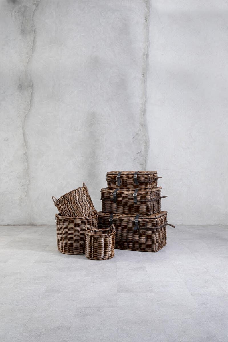 Stacked brown wicker storage baskets with lids and handles on grey floor