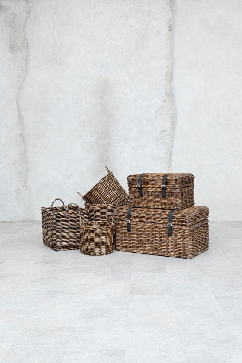 Stacked wicker storage baskets and trunks with handles on light stone floor