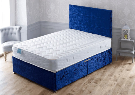 White mattress on blue velvet divan bed with headboard in bright bedroom