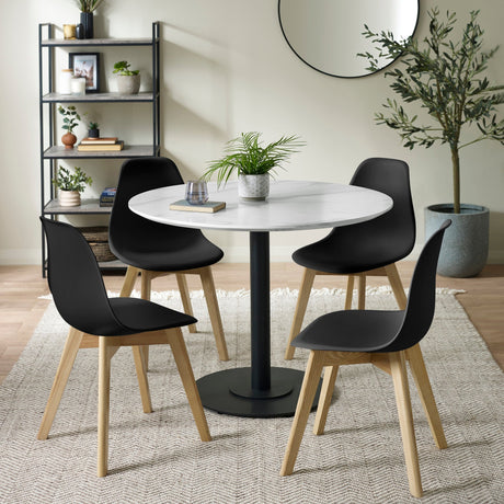 Modern dining table with round white top and four black chairs with wooden legs