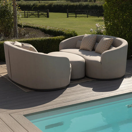 Beige outdoor sofa set with round ottoman and patterned cushions beside swimming pool