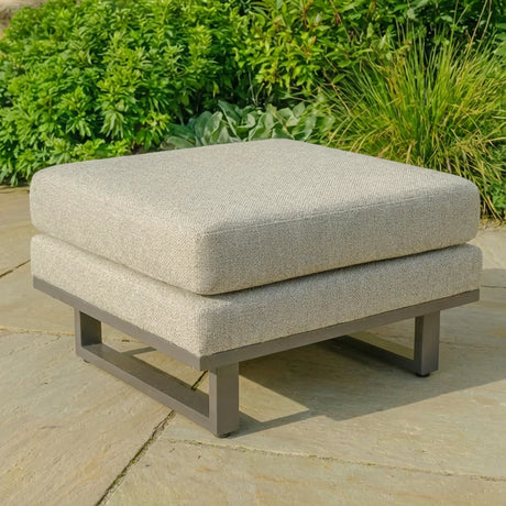 Outdoor footstool with grey cushioned seat and metal frame on stone patio