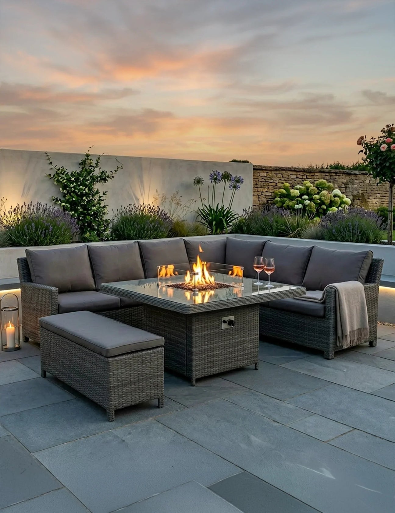Rattan garden sofa set with glass firepit table and grey cushions on patio at sunset
