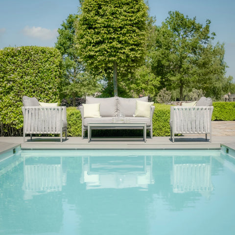 Grey outdoor sofa set with cushions and coffee table by pool, garden background