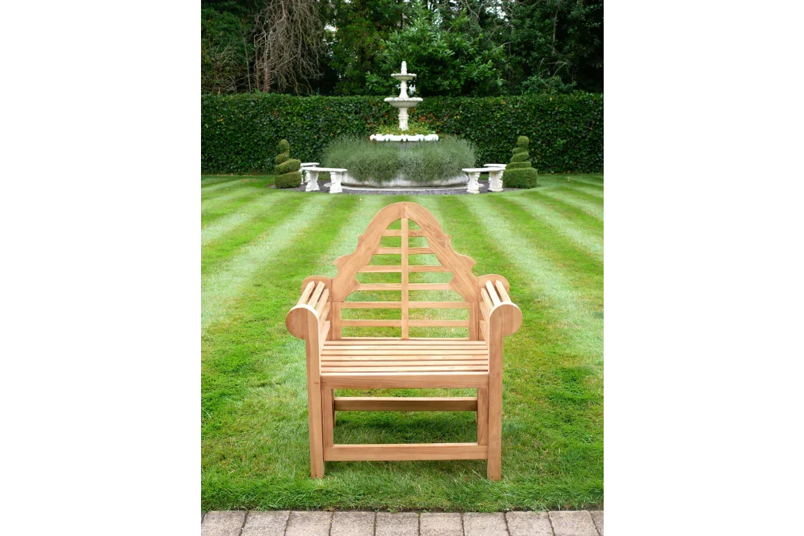 Teak garden bench with arched backrest on striped lawn facing garden fountain