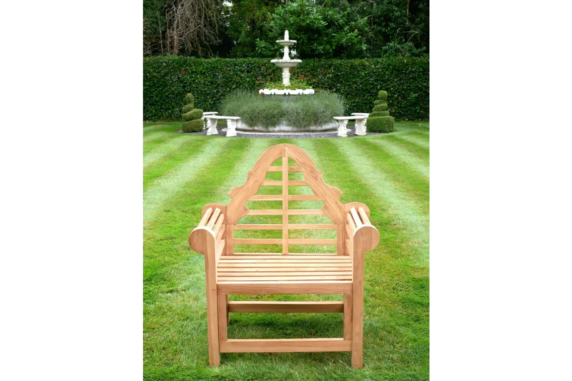 Teak garden bench with decorative backrest on striped lawn facing fountain and benches