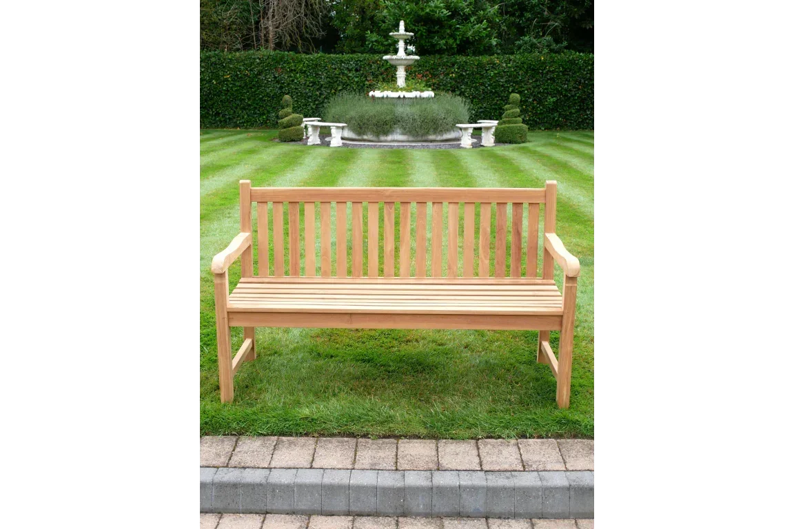 Wooden garden bench with slatted backrest on lawn, fountain and hedges in background