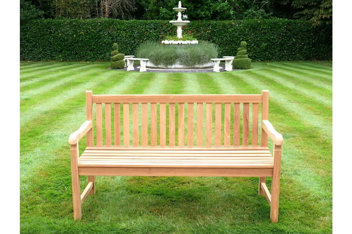 Wooden garden bench with slatted backrest on lawn, fountain and hedges in background