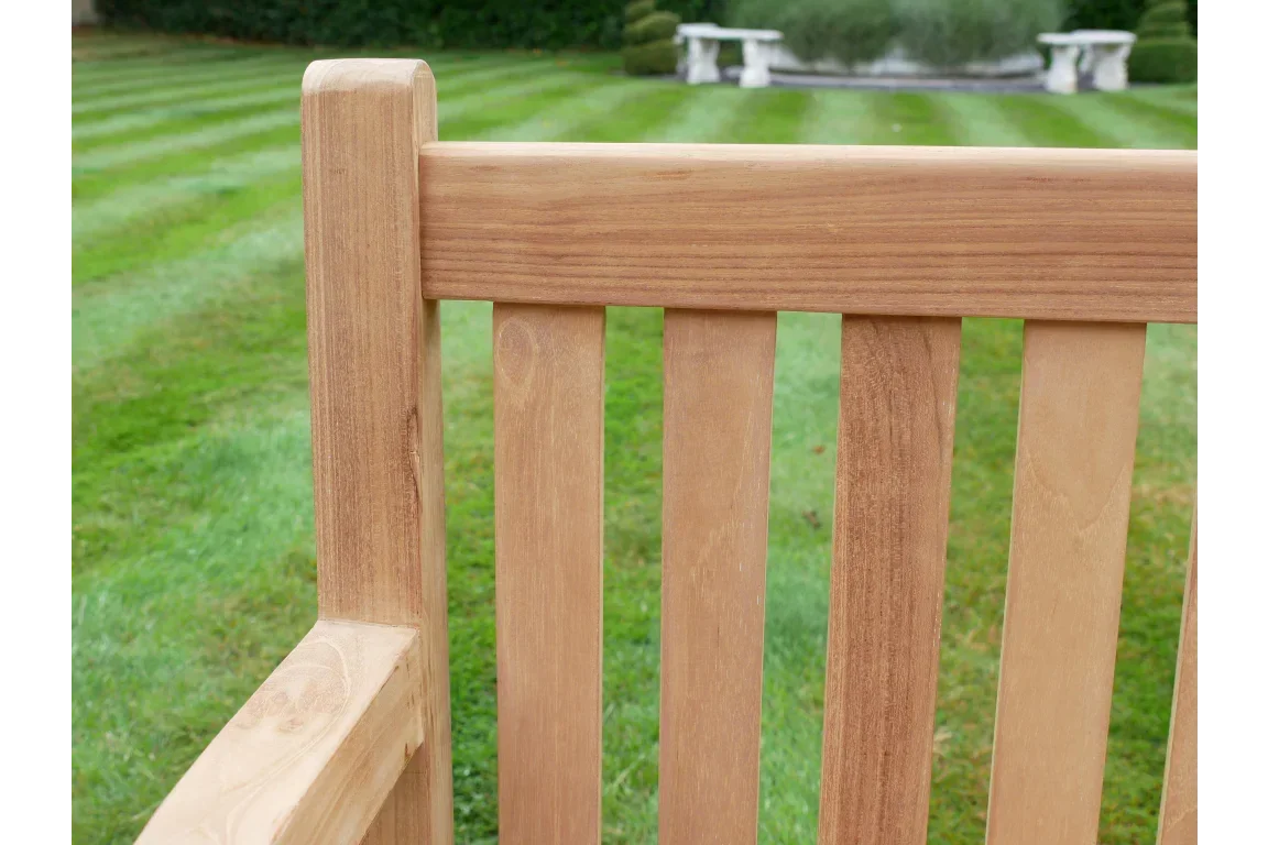 Close up of teak wooden garden bench slats and armrest on grass lawn
