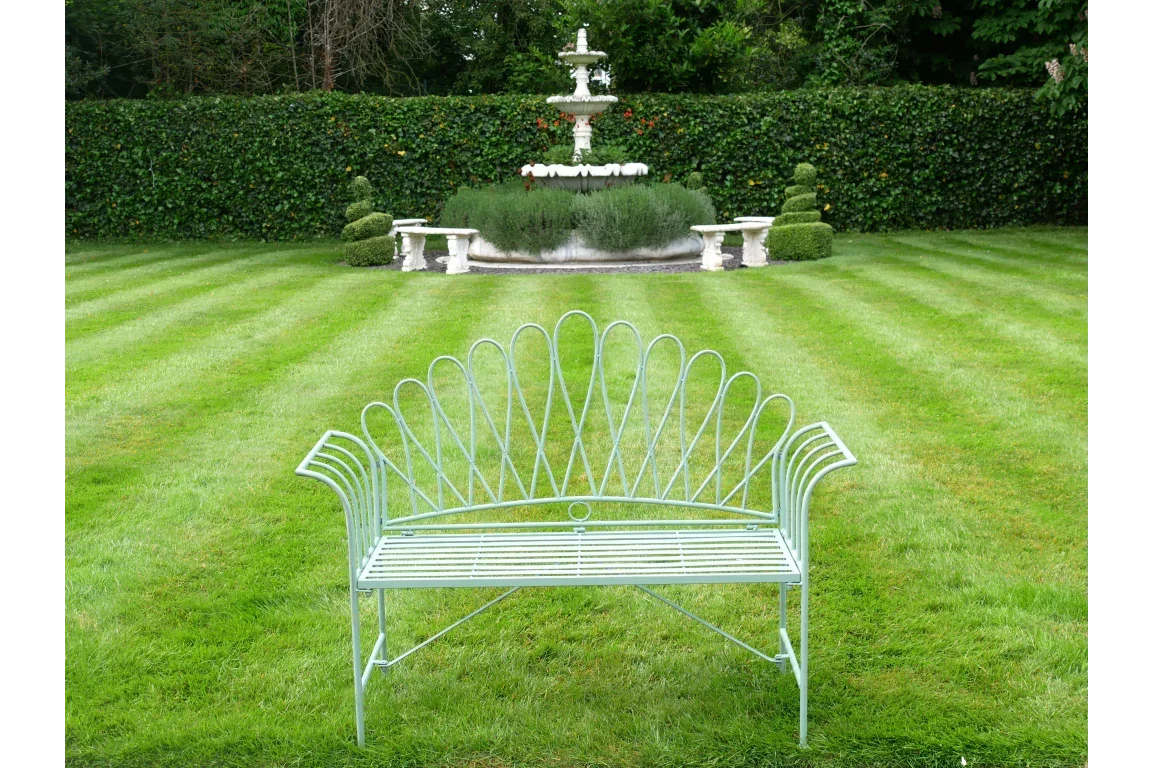 Metal garden bench with decorative backrest on striped lawn facing fountain