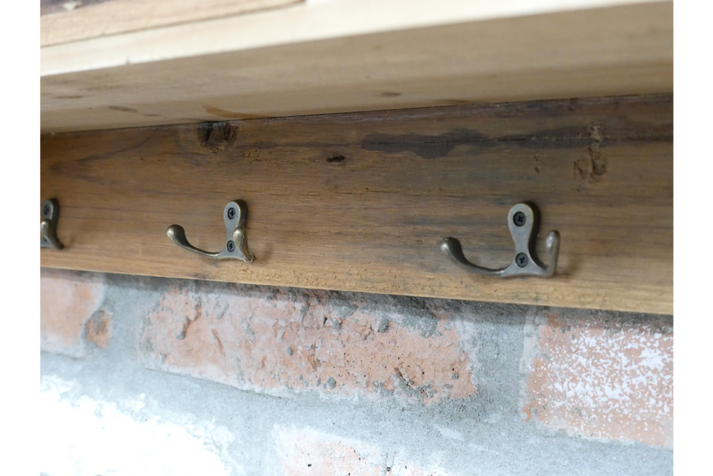 Wooden wall unit with three metal double hooks mounted on a brick wall, side angle view.