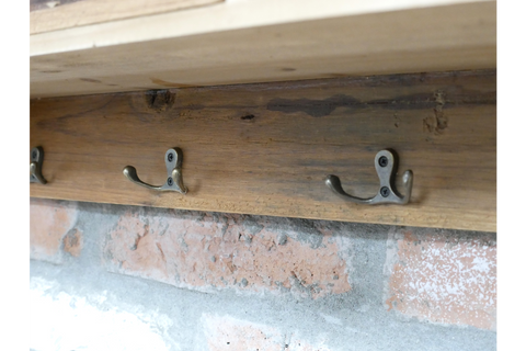 Wooden wall unit with three metal double hooks mounted on a brick wall, side angle view.