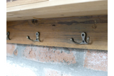 Wooden wall unit with three metal double hooks mounted on a brick wall, side angle view.