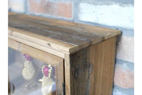 Close-up angled view of rustic wooden wall unit with glass door in front of brick wall background.