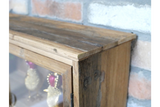 Close-up angled view of rustic wooden wall unit with glass door in front of brick wall background.