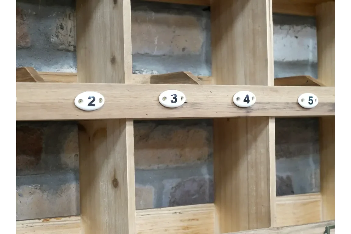 Wooden pigeon hole storage unit with numbered compartments against brick wall