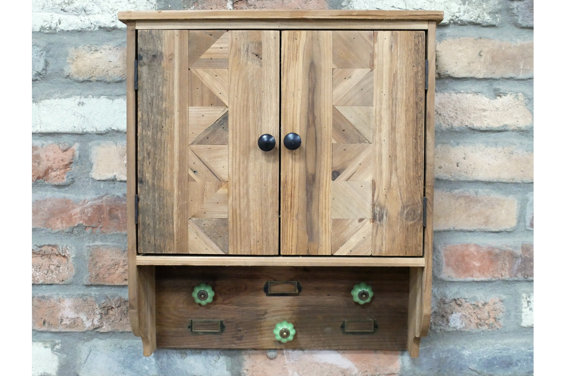 Wooden wall-mounted storage unit with two doors and five green decorative hooks, front view against brick wall.