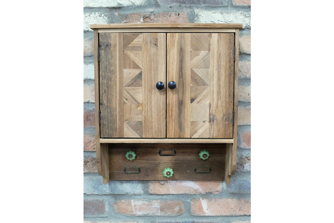 Wooden wall unit with geometric patterned doors, black knobs, and three green ceramic hooks, mounted on brick wall.