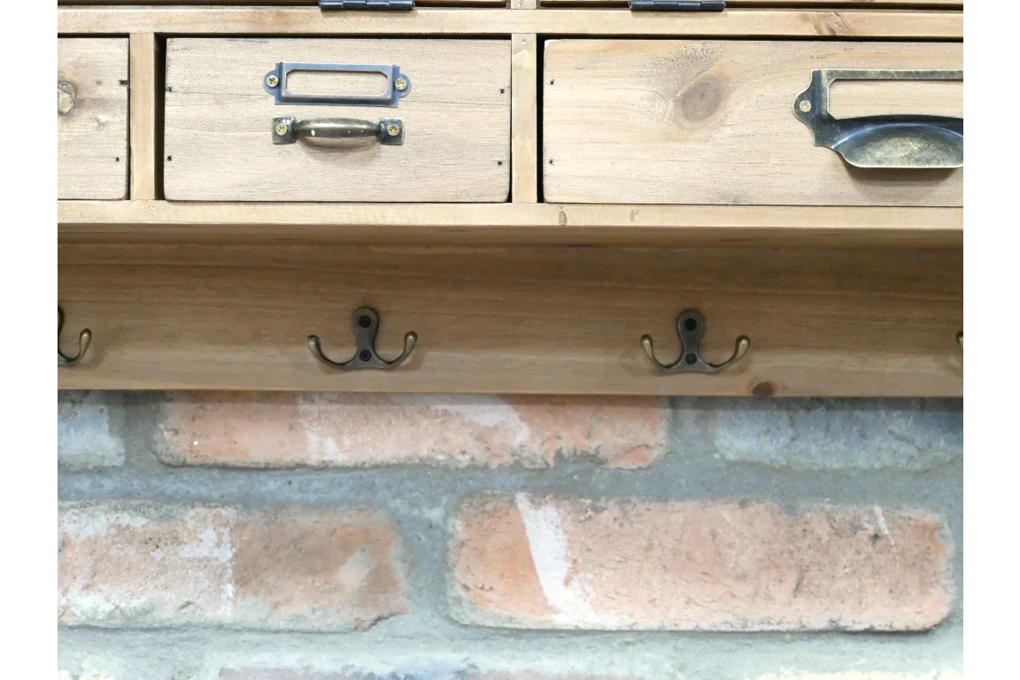 Wooden wall-mounted coat rack with drawers and brass hooks against brick background
