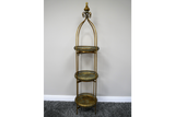 Tall 3 tier metal shelves with decorative round trays in gold and green, standing on a carpeted floor against a plain wall.