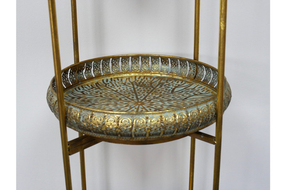Close-up of a round decorative metal tier with gold ornate detailing on a 3-tier shelving unit.