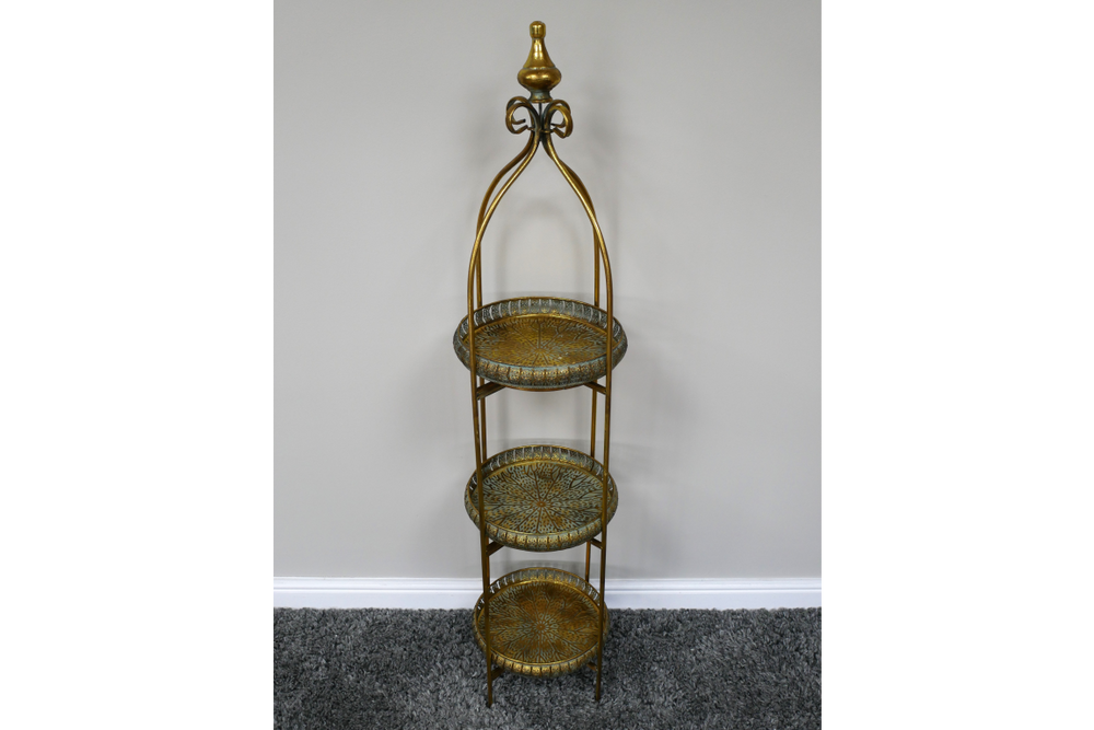 Tall 3 tier metal shelves with decorative round trays in gold and green finish, standing on gray carpet.