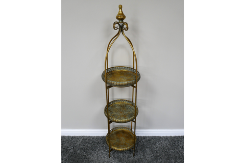 Tall 3 tier metal shelves with decorative round trays in gold and green finish, standing on gray carpet.