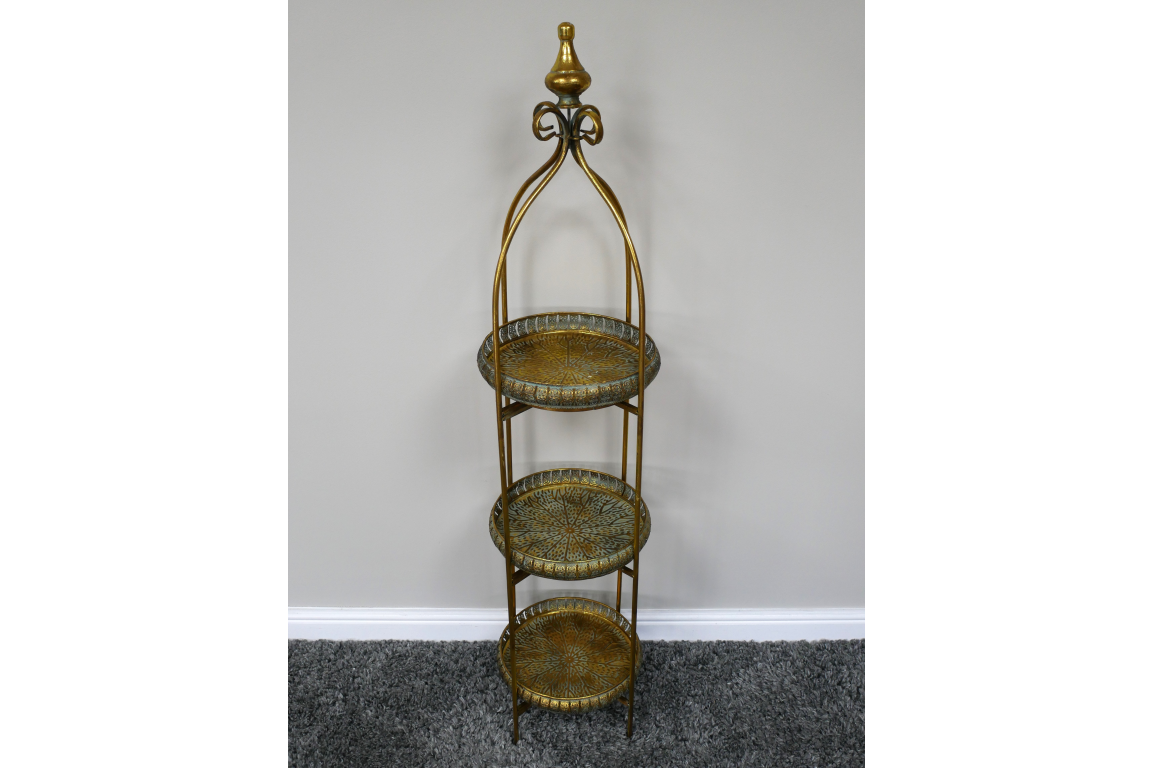 Tall 3 tier metal shelves with decorative round trays in gold and green finish, standing on gray carpet.