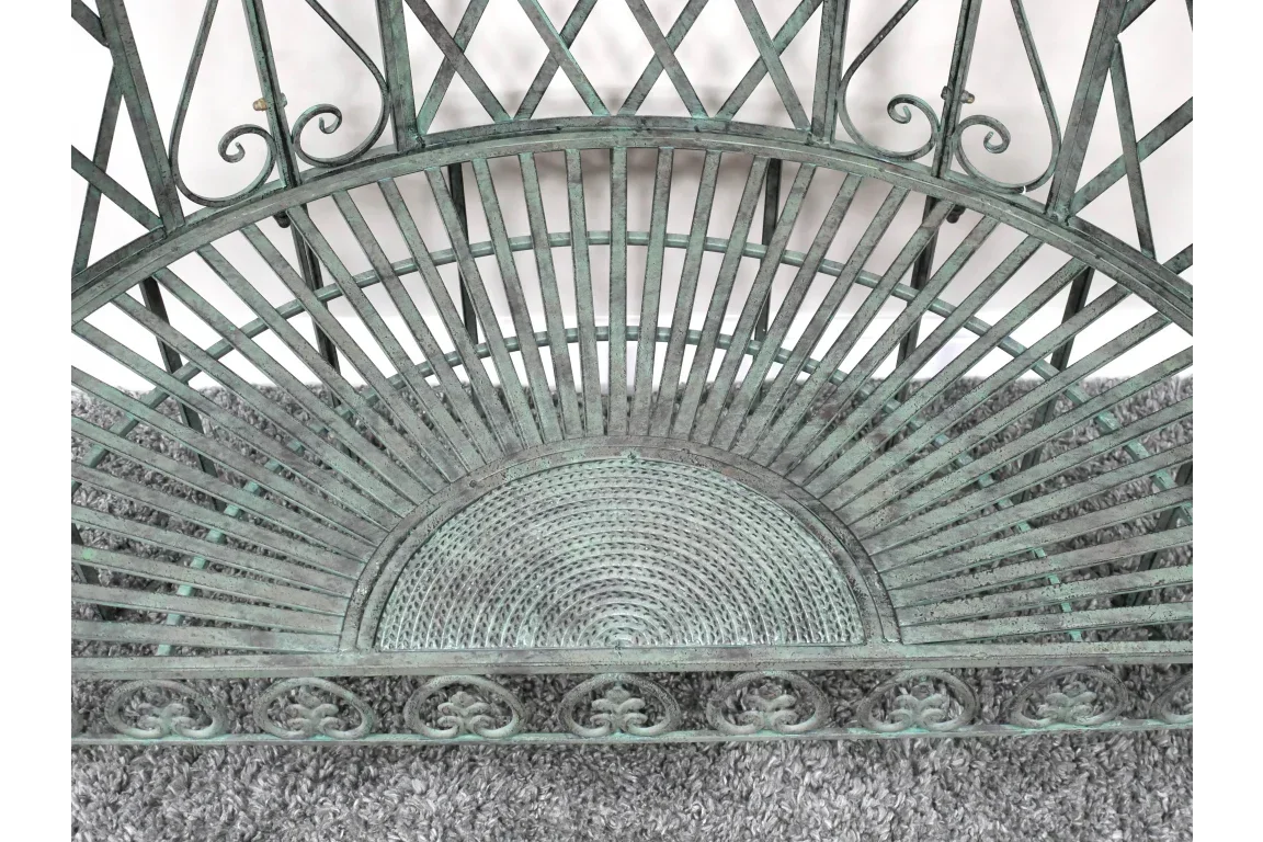 Green metal garden bench with decorative backrest and woven style seat on grey rug
