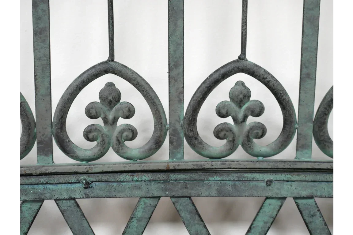 Green wrought iron gate with fleur-de-lis design and weathered finish detail