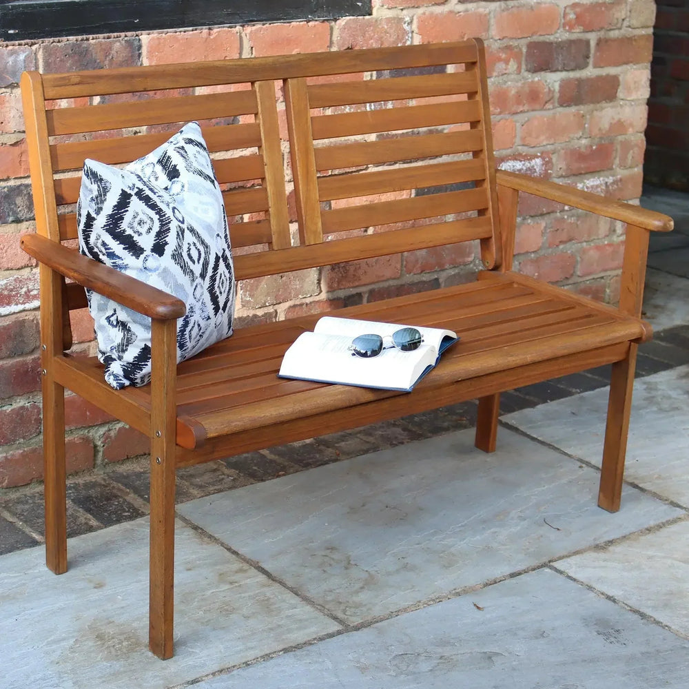 Wooden garden bench with slatted backrest, patterned cushion, and book on patio